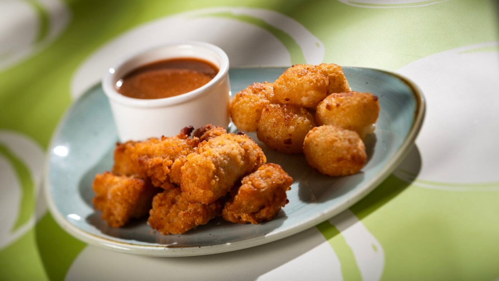 2026WDWCoolKidsSummerTreats7 Fantasy Land News Plate of crispy fried chicken bites with a cup of reddish dipping sauce on a blue plate in a bright setting