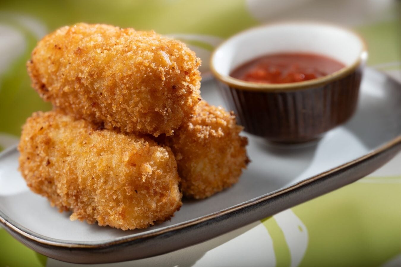 2026WDWCoolKidsSummerTreats81620x1080 Fantasy Land News Golden crispy croquettes stacked on a white plate with a small cup of red dipping sauce nearby