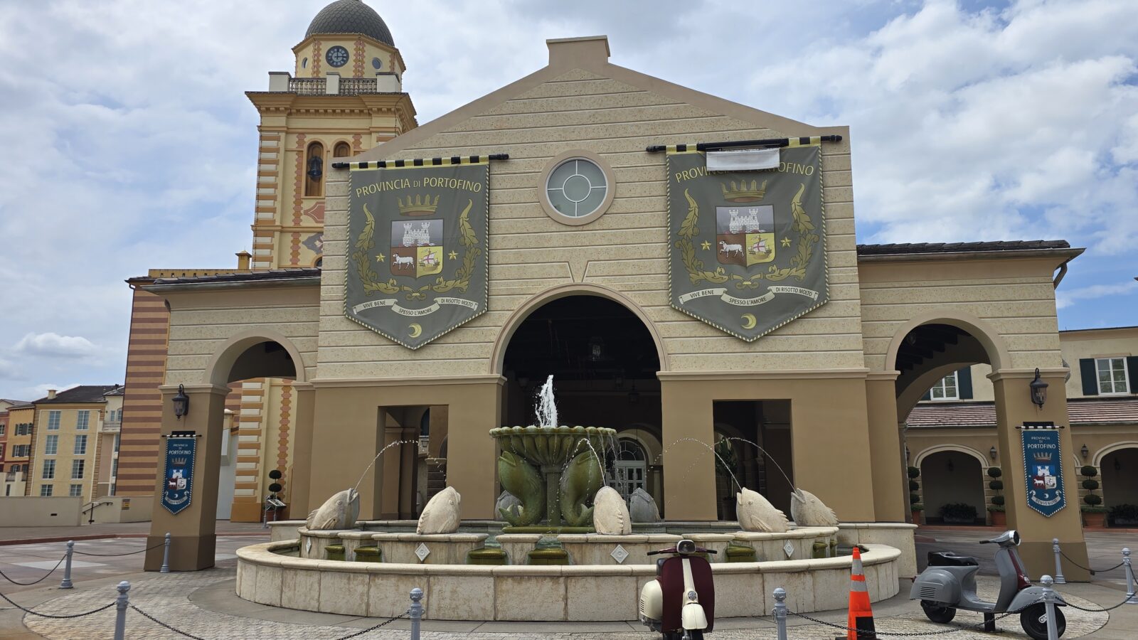 Facade of a beige civic building with two large banners reading Provincia di Portofino and a circular window front fountain in the foreground on a sunny day