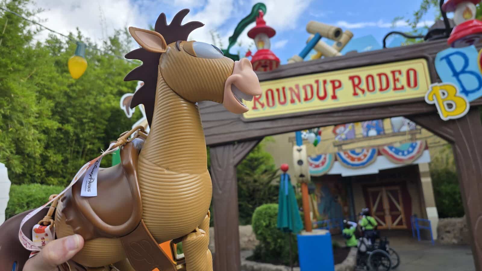 Close up of a brown horse statue with reins held by a person at the Roundup Rodeo sign in the background