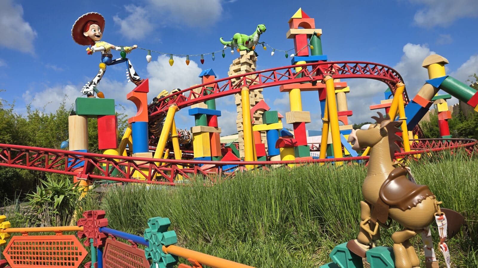 Colorful theme park roller coaster with Woody and Rex figures perched on the red track against a blue sky toys and blocks throughout the structure