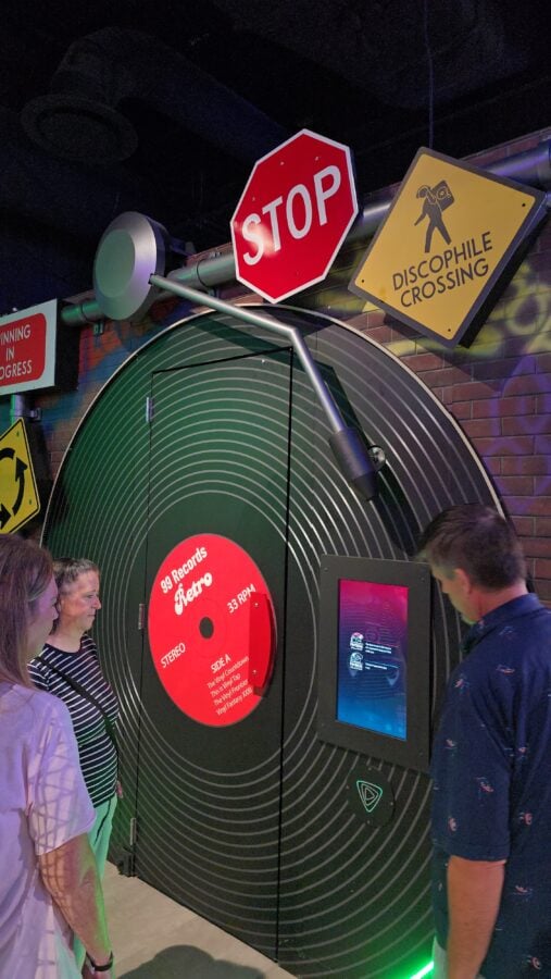 Oversized STOP sign and Discophile Crossing sign above a large circular vinyl record display at a retro music exhibit