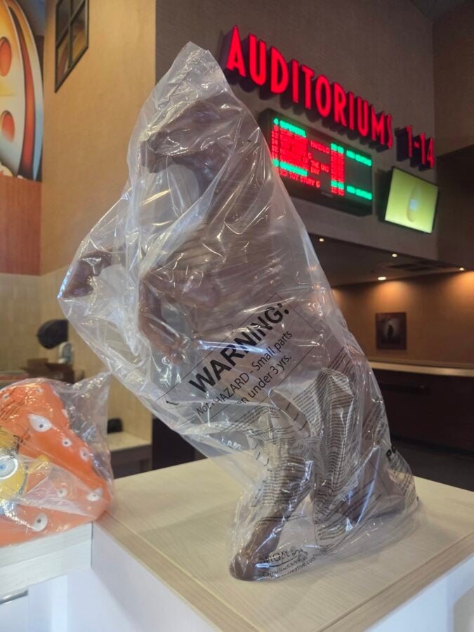 Plastic wrapped item on a counter in a theater lobby with a bright red AUDITORIUMS sign in the background