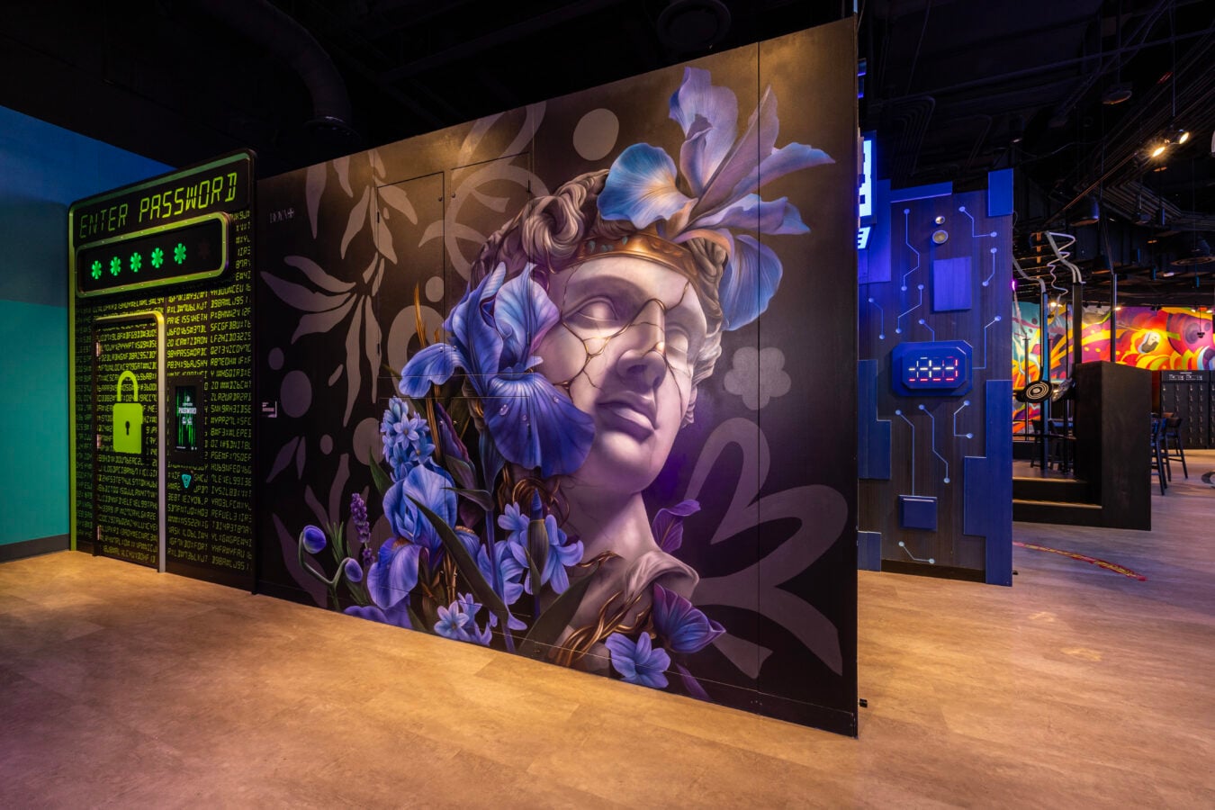 Large mural of a womans face with blue flowers on a dark wall in a tech themed space by neon signage and circuitry motifs