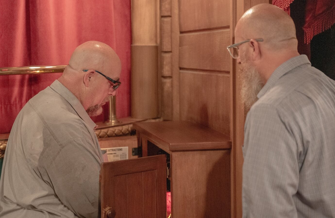 Bob at work supporting operations across Walt Disney World Resort Fantasy Land News Two bald men in gray shirts facing each other at a wooden cabinet with a red curtain behind them