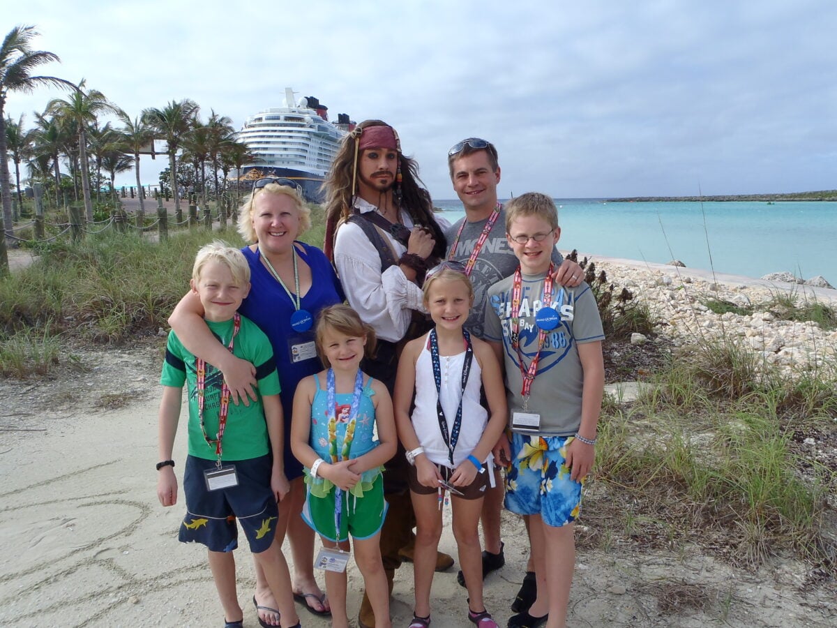Family group posing on a beach with a pirate costumed man and a cruise ship in the background Informative
