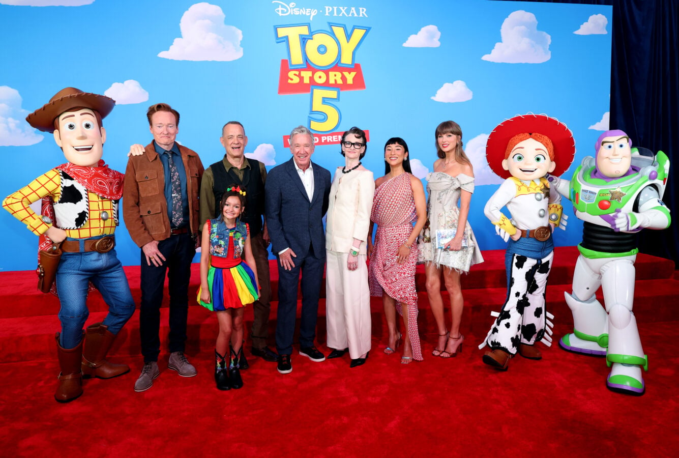 Toy Story 5 Los Angeles World Premiere Fantasy Land News Group of adults and a child posing on a red carpet with Toy Story 5 backdrop alongside life size Woody Jessie and Buzz Lightyear characters