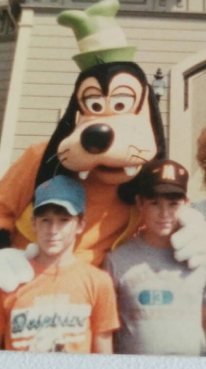 Michael and Bob during their first visit to Walt Disney World Fantasy Land News Goofy mascot posing with two boys outdoors one wears an orange shirt and blue cap the other a gray shirt and brown cap