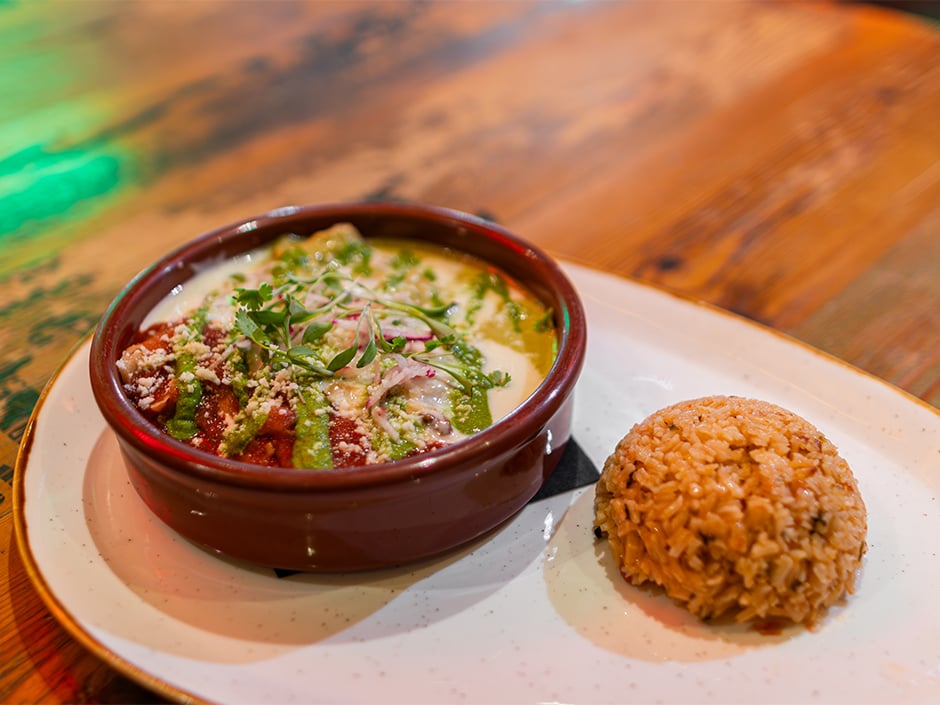 Creamy soup in a brown bowl topped with herbs and grated cheese with a side of seasoned rice on a white plate