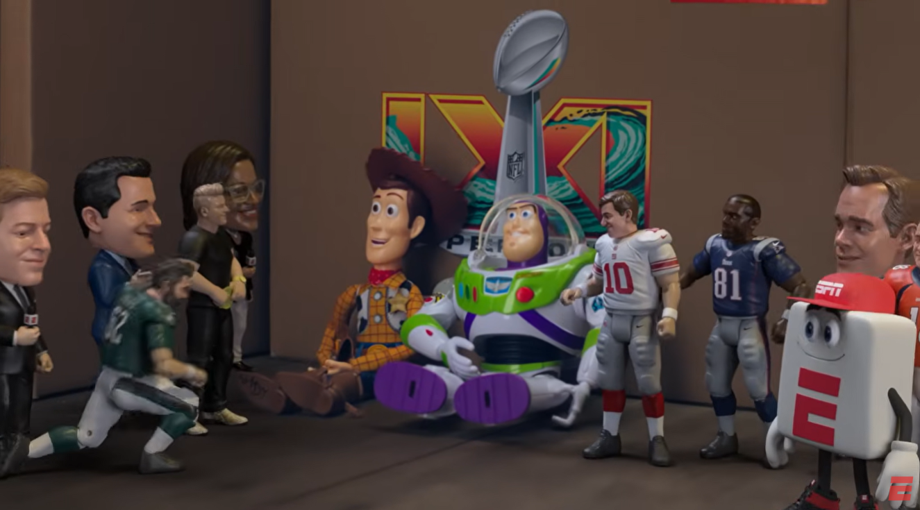 Cartoon sports characters and Toy Story figures including Woody and Buzz Lightyear gather around a tall trophy in a studio setting