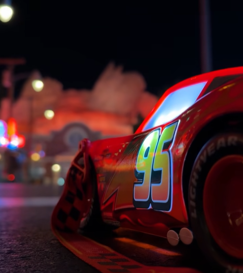 Nighttime race car with number 95 on a red body close up shot focusing on the side of the car with blurred background lights behind it