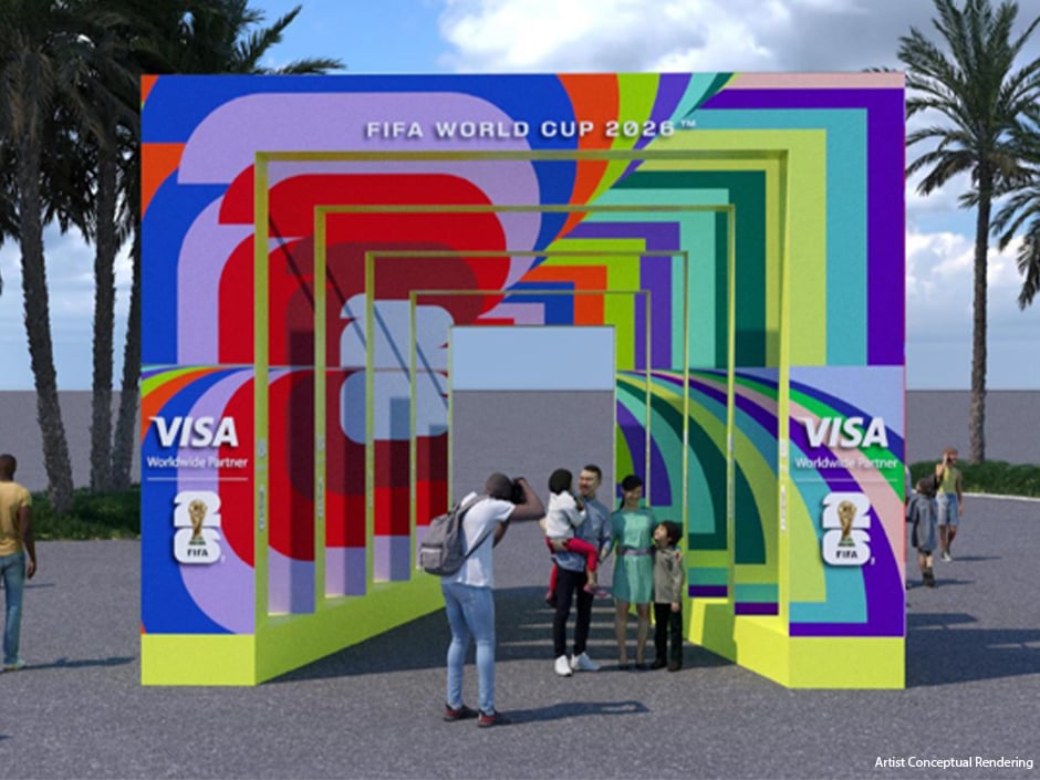 Colorful geometric arch installation advertising FIFA World Cup 2026 with Visa logos and visitors posing nearby on a paved area by palm trees