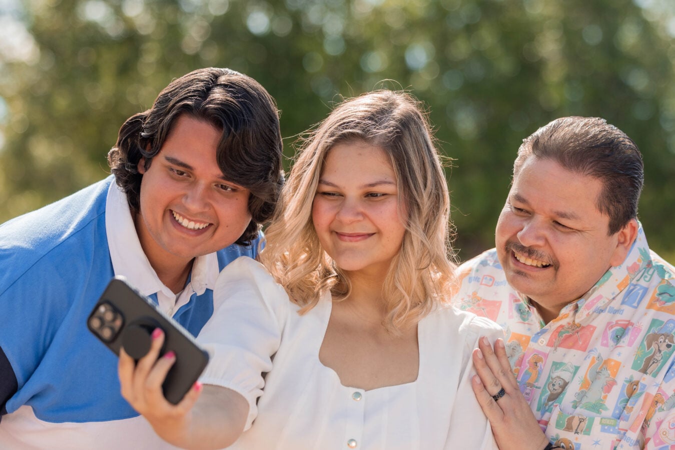 Three friends posing for a selfie outdoors smiling at the camera held by the person on the left