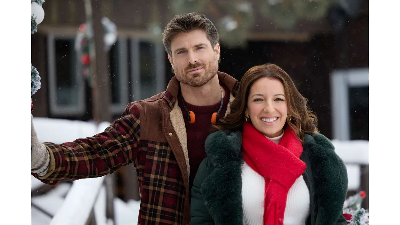 Smiling couple in winter coats posing outdoors in the snow with a red scarf and plaid jacket