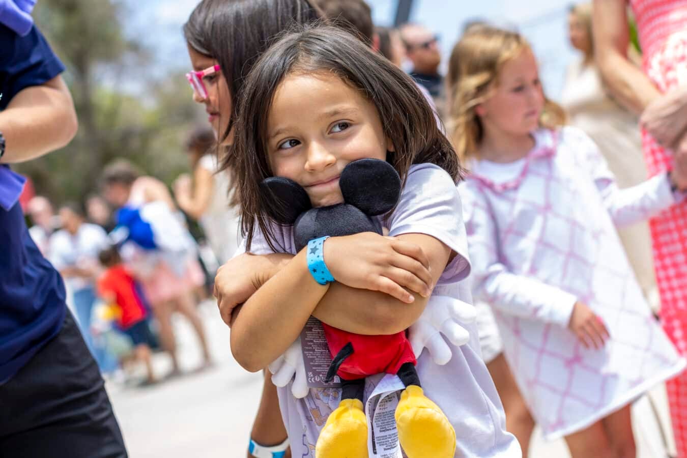 Young girl hugs a black plush penguin while surrounded by a crowd at an outdoor event