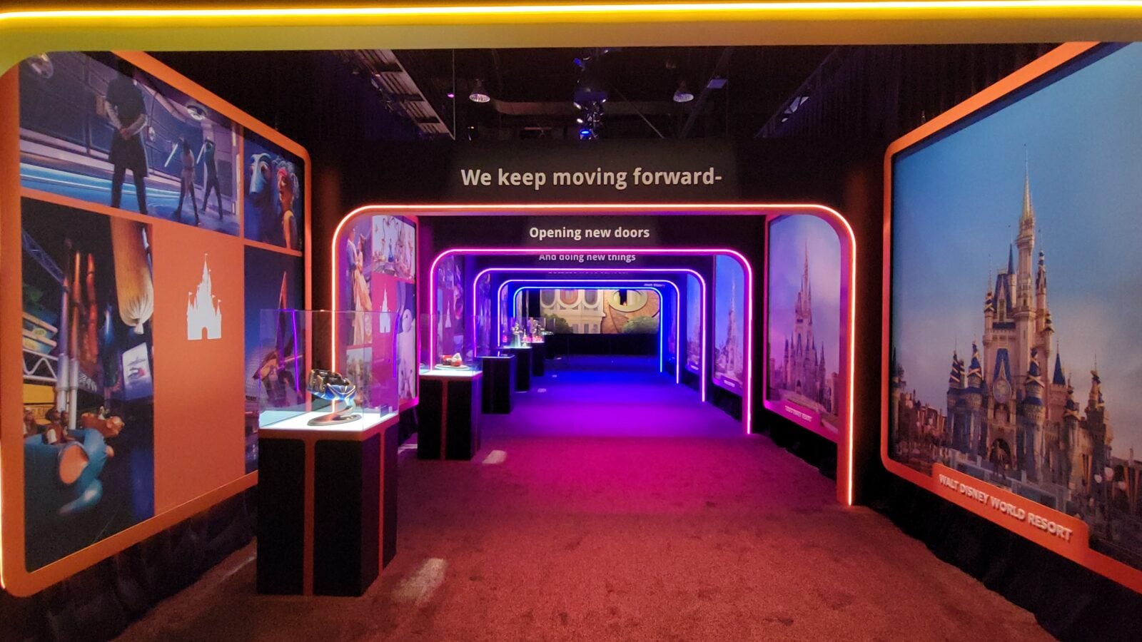 Disney themed exhibit hallway with neon pinkpurpleorange arches and large wall panels displaying Disney imagery read We keep moving forward