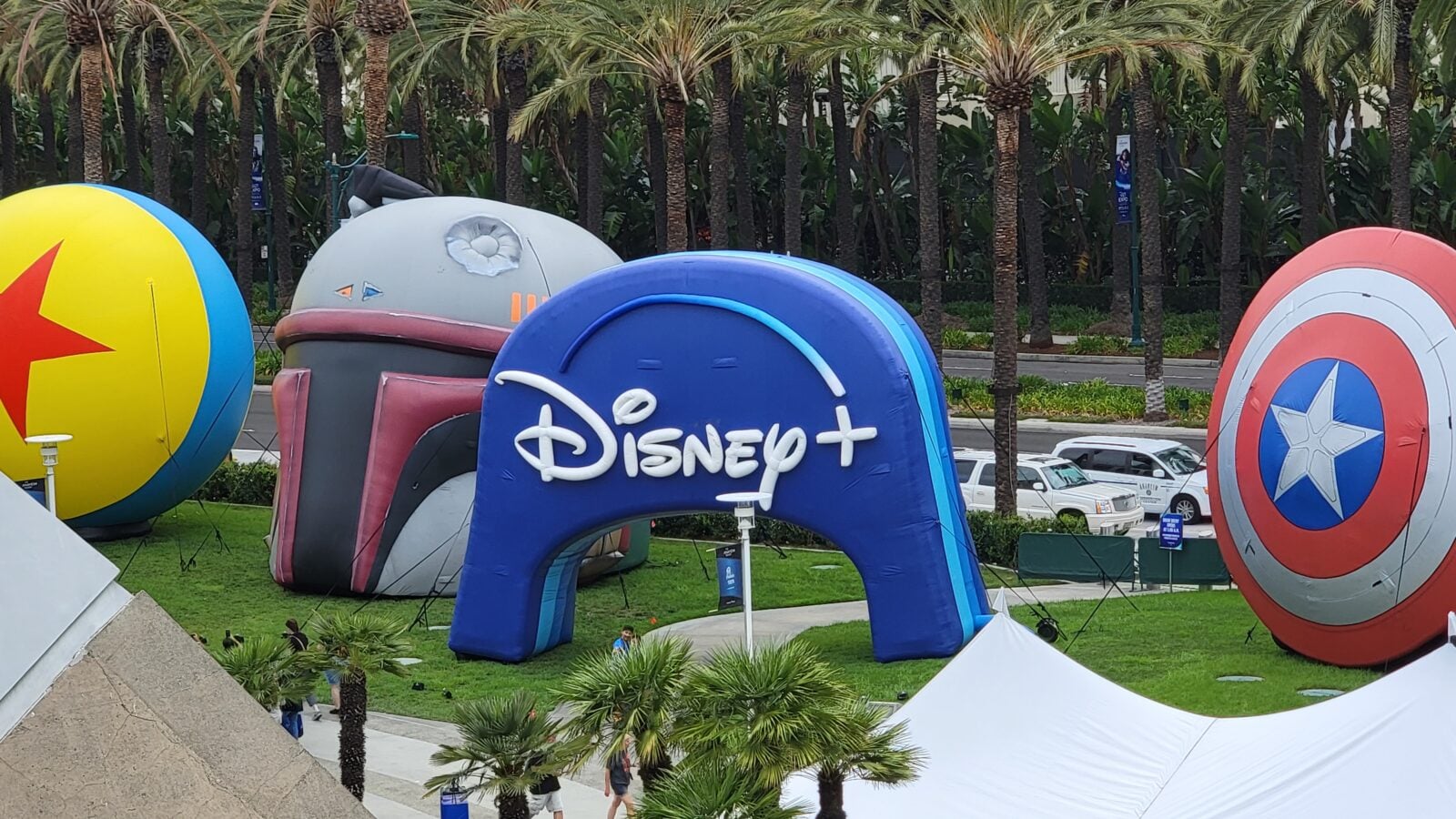 Colorful inflatable shapes including a Disney+ arch and a Captain America shield set among palm trees at an outdoor festival