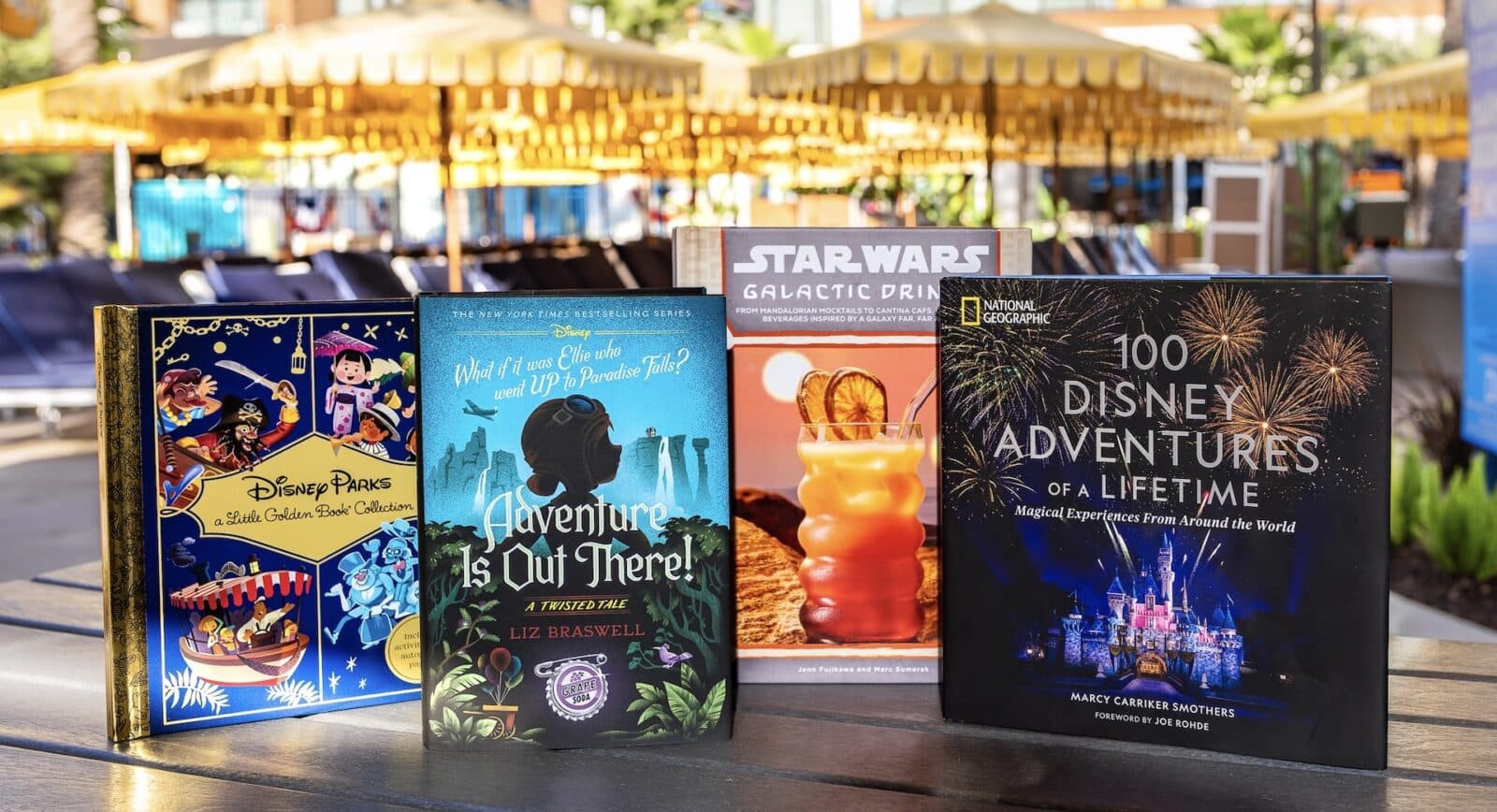 Row of Disney themed books displayed on a wooden table outdoors under yellow umbrellas