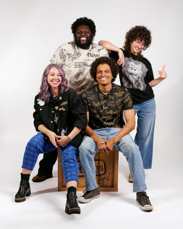 Four friends posing in a studio smiling and relaxed with one seated on a wooden crate and others standing behind himaround