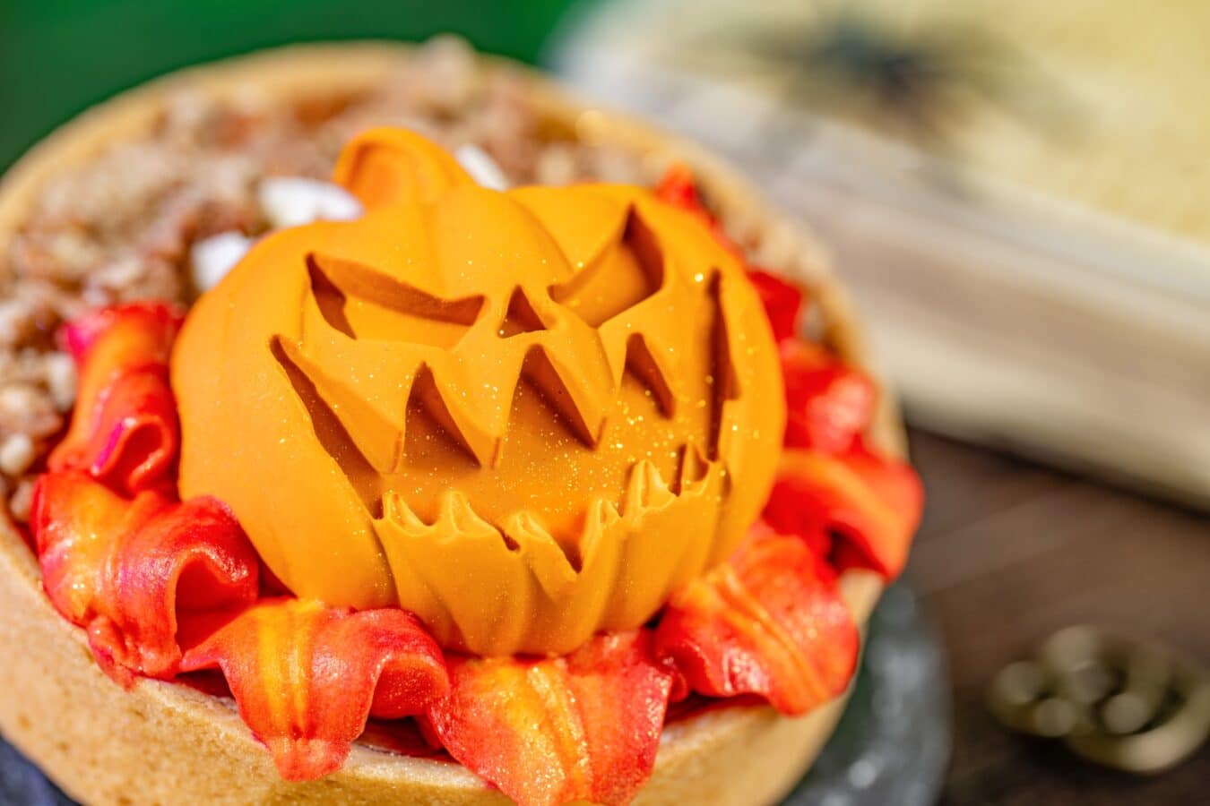 Close up of a carved orange Halloween pumpkin decoration atop a pastry with orange frosting petals around it