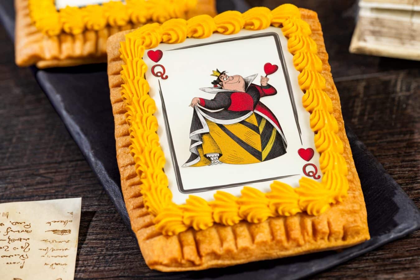 Cake with a Queen of Hearts playing card topper framed by bright yellow frosting on a rectangular pastry crust