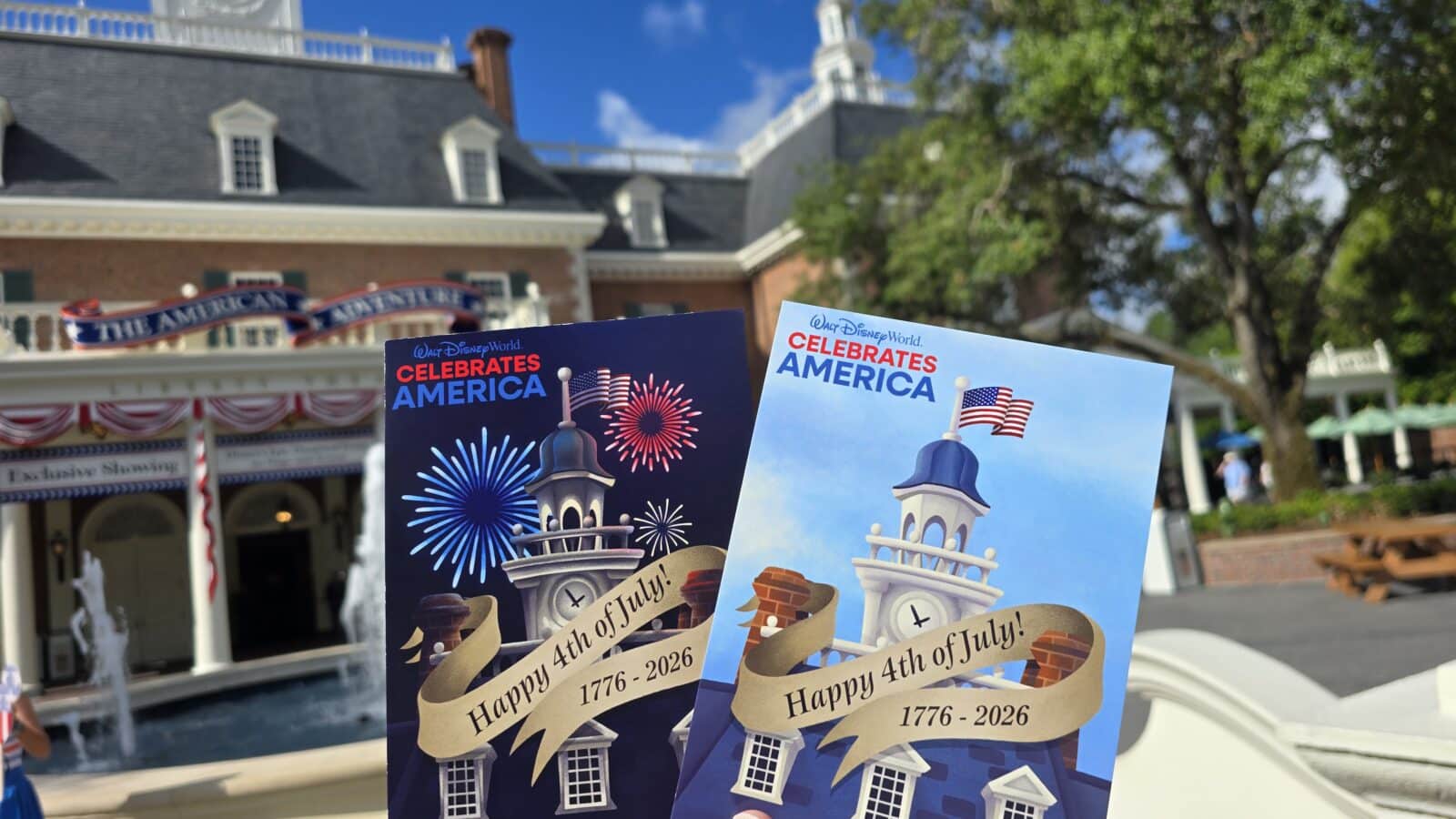 Two US themed July 4th brochures held up in front of a Disney World backdrop with fireworks illustrations and flags behind them 17762026