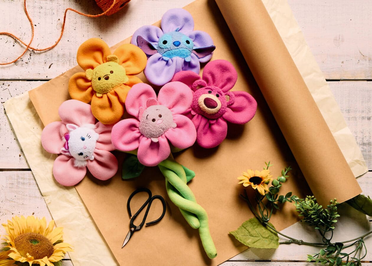 Bright stuffed fabric flowers in yellow pink purple with smiling faces arranged on craft paper beside scissors and sunflowers
