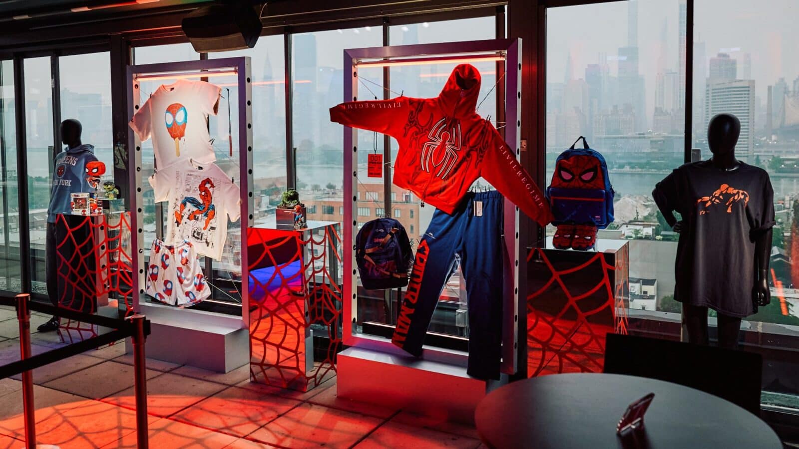 Store window display of Spider Man themed clothing and accessories on mannequins with a city skyline in the background