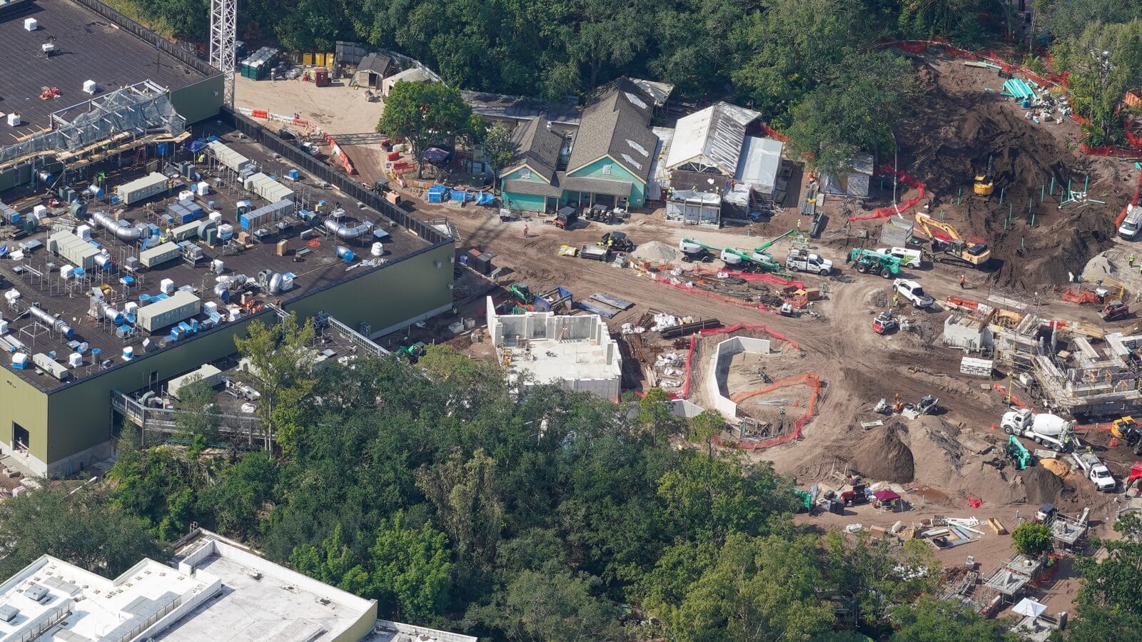 Aerial view of a construction site with cranes equipment and dirt piles beside green trees