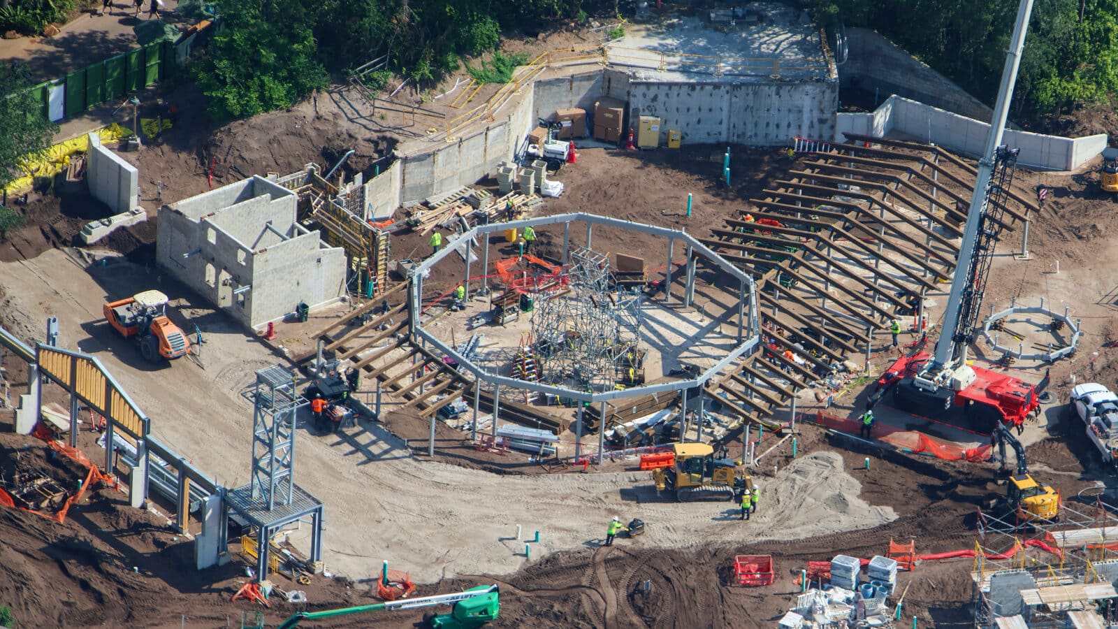 Construction site with a circular steel framework being assembled workers in high visibility vests and concrete walls surrounding the area
