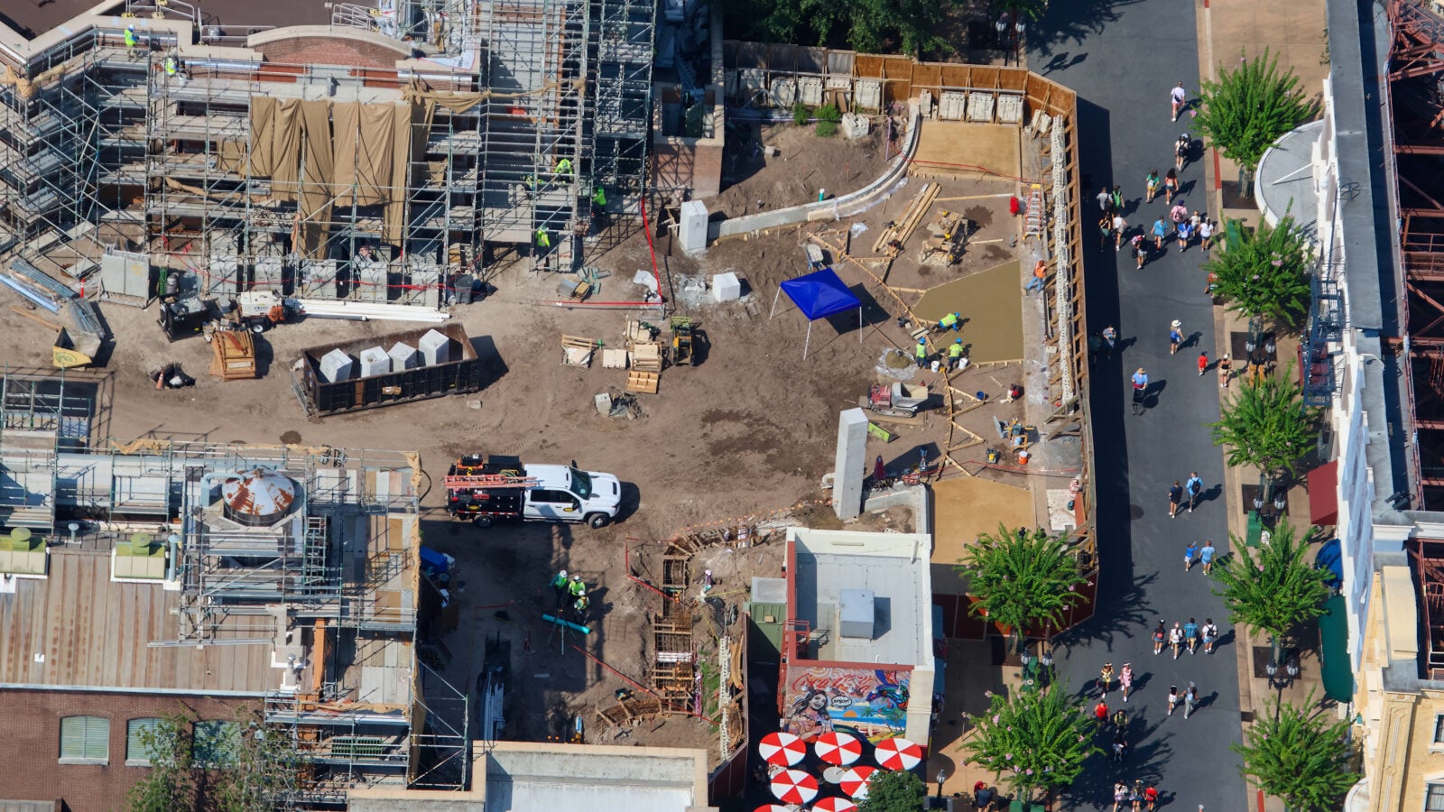 Aerial view of a busy construction site with scaffolding workers in safety vests and a surrounding street with pedestrians nearby