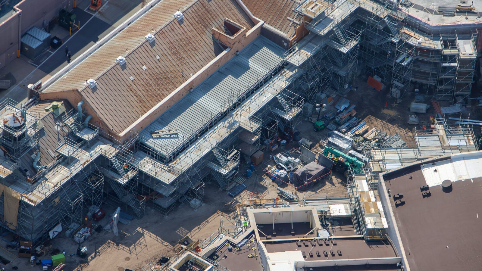 Aerial view of a large construction site with extensive scaffolding surrounding a multi level structure under a brown tiled roof and concrete platforms
