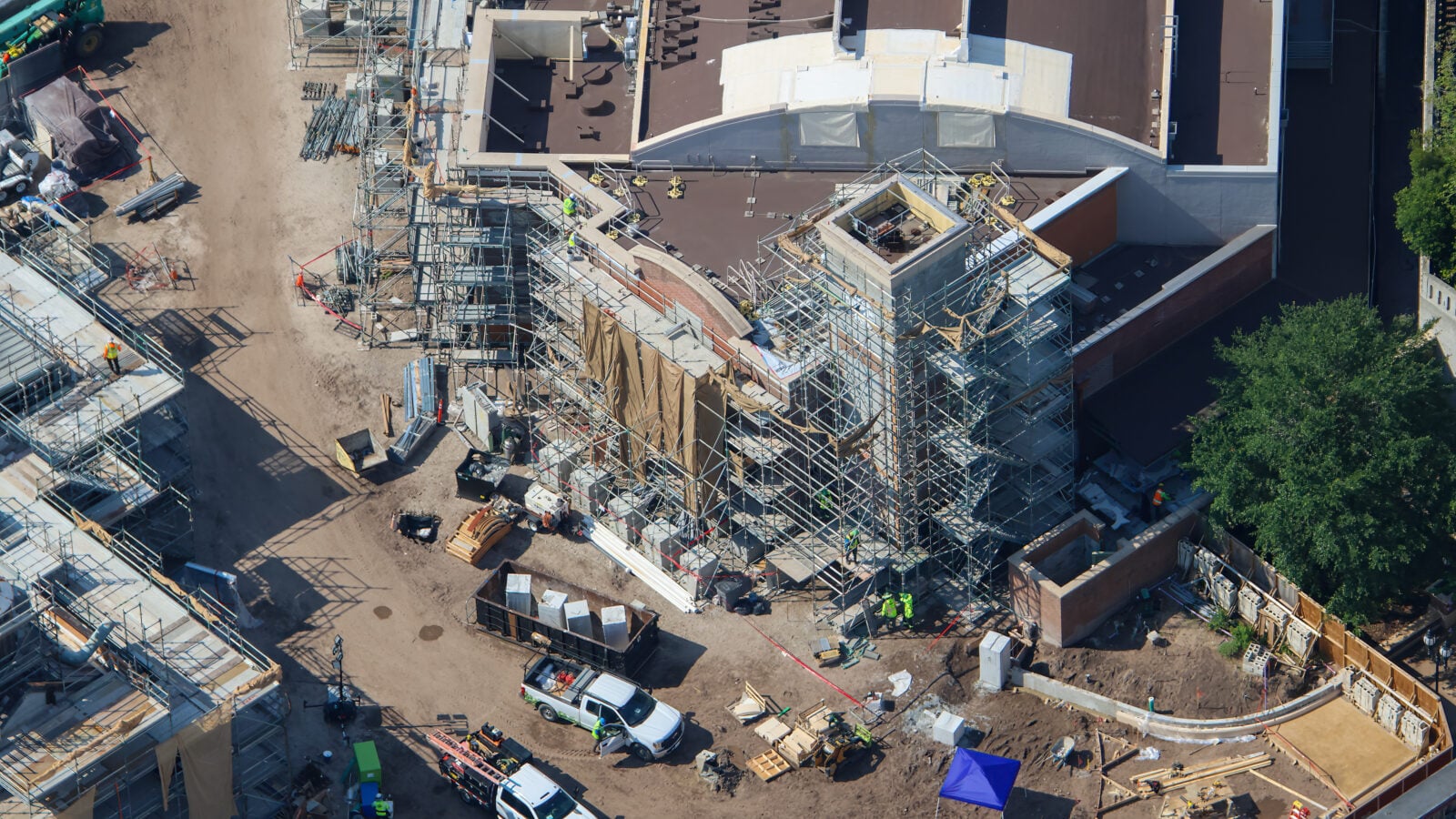 Aerial view of a busy construction site with scaffolding surrounding a curved building and workers in safety gear