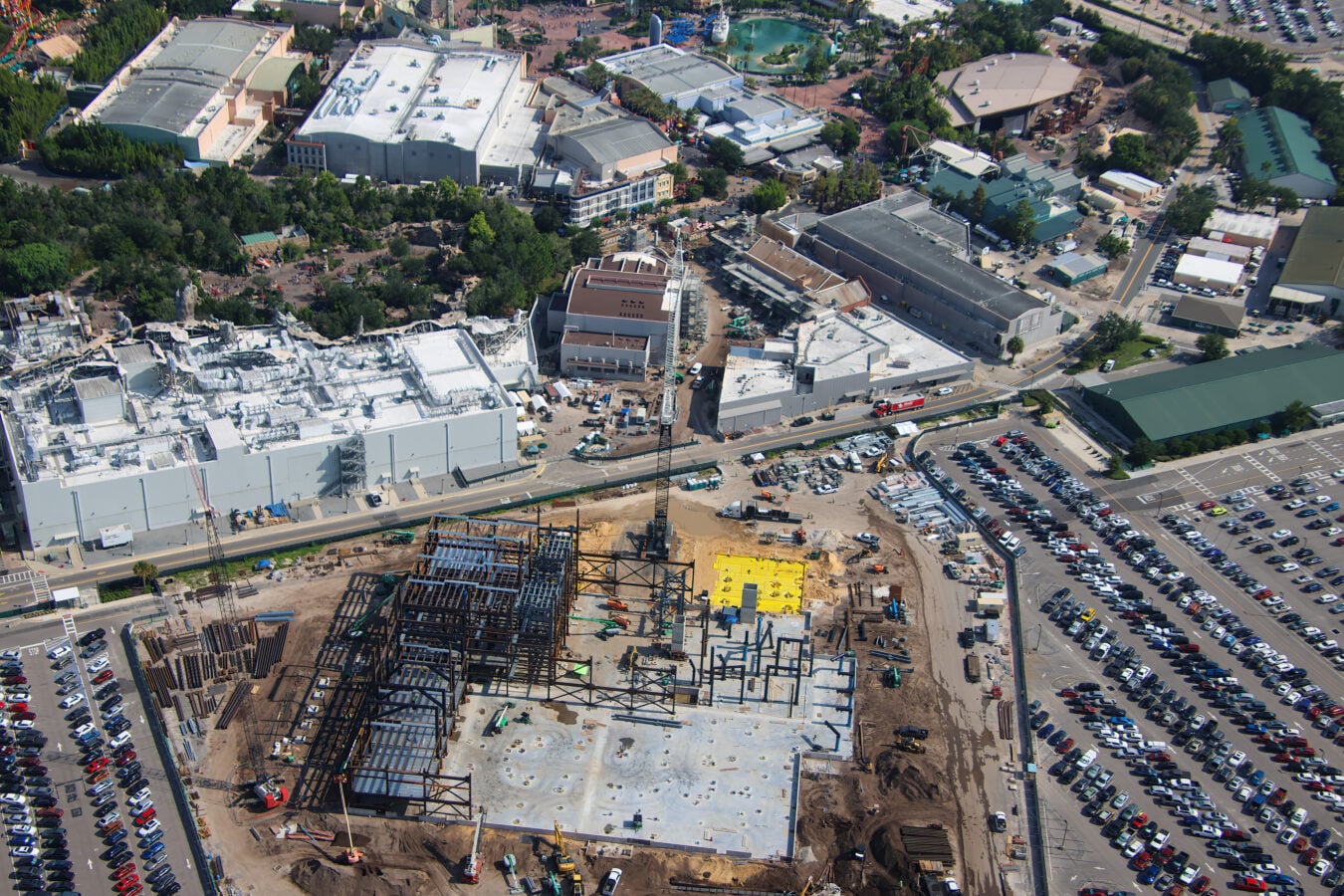 Aerial view of a busy construction site with steel scaffolding concrete buildings and surrounding parking areas