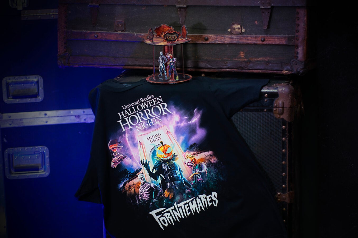 Poster for Universal Studios Halloween Horror Nights featuring spooky characters and pumpkins on a stage against a wooden backdrop