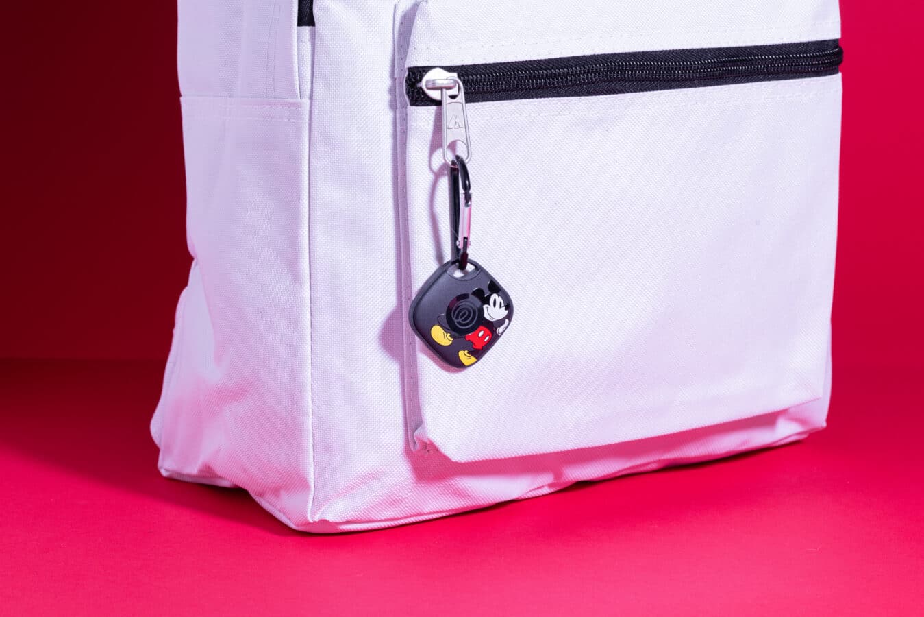 White backpack zipper with a Mickey Mouse keychain hanging from it set against a pink background