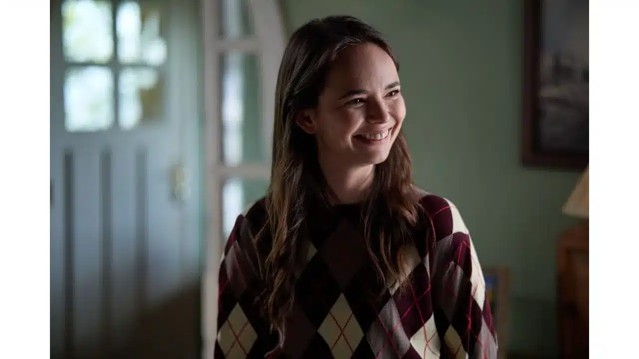 Say Oui To Romance in Paris Is Always a Good Idea on Hallmark+ Review Fantasy Land News Woman with long brown hair smiling wearing burgundy and cream argyle sweater indoors