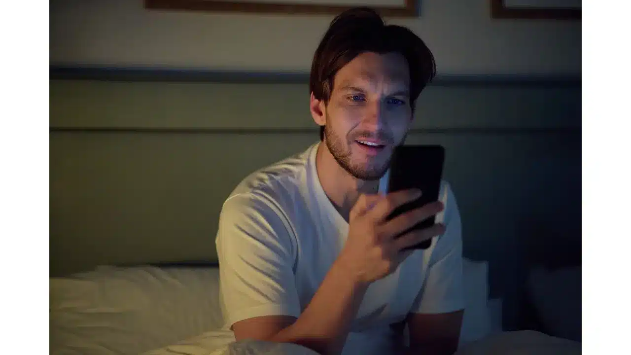 Say Oui To Romance in Paris Is Always a Good Idea on Hallmark+ Review3 Fantasy Land News Young man lying in bed at night looking at his smartphone with a soft glow on his face