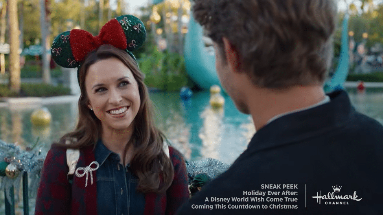 Woman wearing festive Minnie Mouse ears smiles at a man in a park by a decorative fountain Hallmark Channel promo text visible