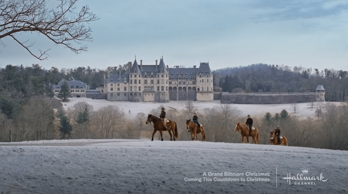 Snow covered landscape with a large castle like mansion in the background and riders on horses in the foreground Hallmark Channel promo text visible at bottom right