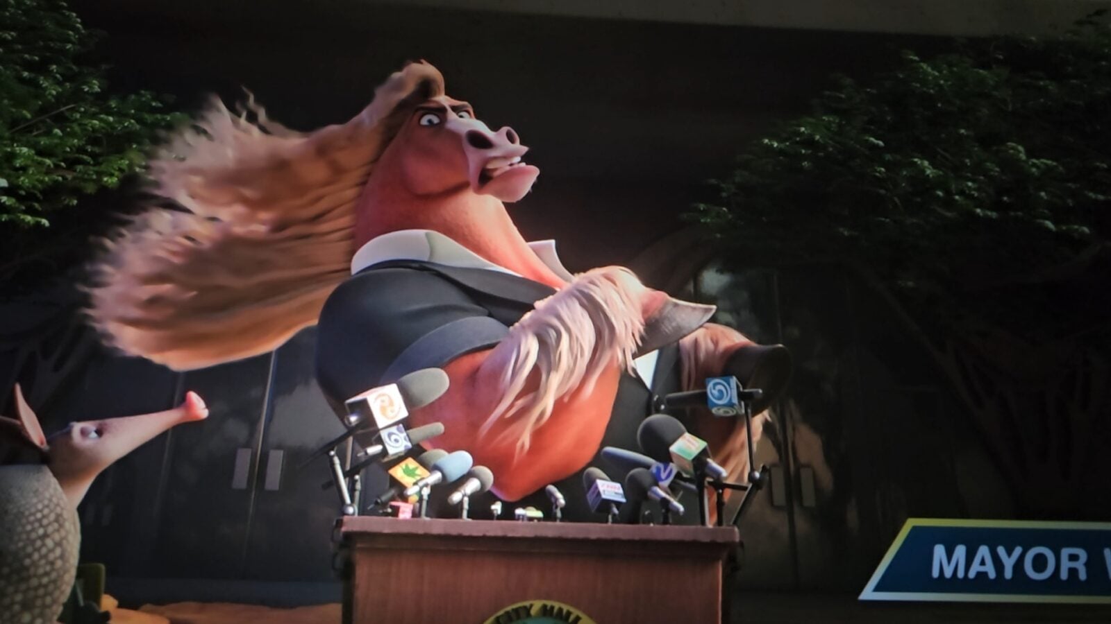 Giant cartoon rooster mascot addressing reporters at a podium with many microphones in front of it