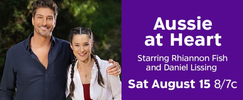 Smiling man and woman stand next to a purple poster that reads Aussie at Heart starring Rhiannon Fish and Daniel Lissing with Sat Aug 15 87C shown