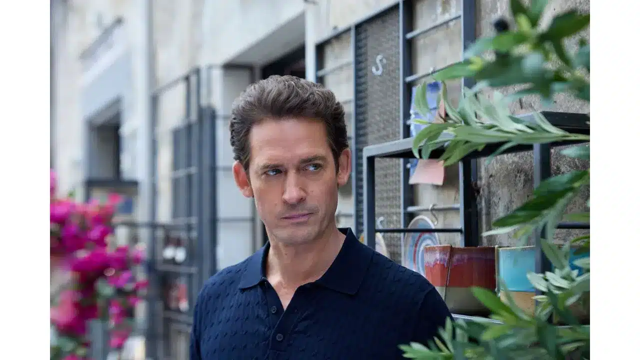 Man in a navy polo standing on a city street with greenery and storefronts in the background