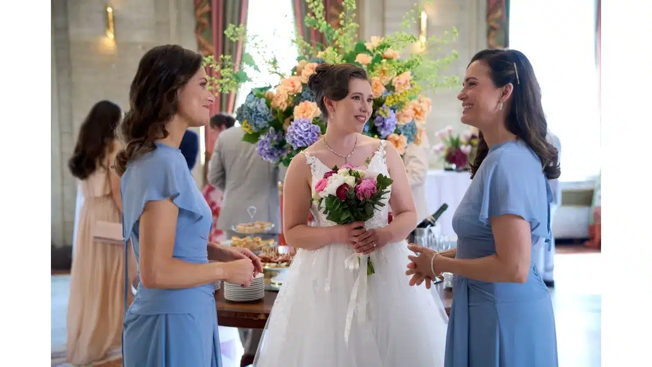 Bride in a white wedding gown holds a bouquet flanked by two bridesmaids in blue at a wedding reception