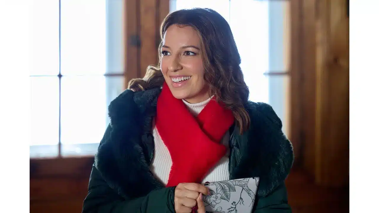 snowbound2 Fantasy Land News Smiling woman in a green coat with a red scarf holding a floral notebook indoors by a window