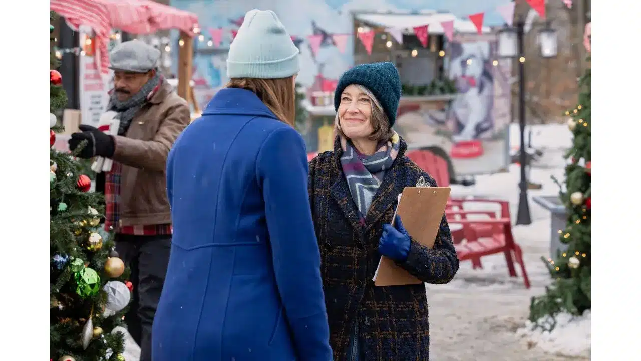 Two women in winter coats chat at a festive outdoor holiday market one holds a clipboard30 or simply Two women in winter wear chat at a festive outdoor market one holding a clipboard