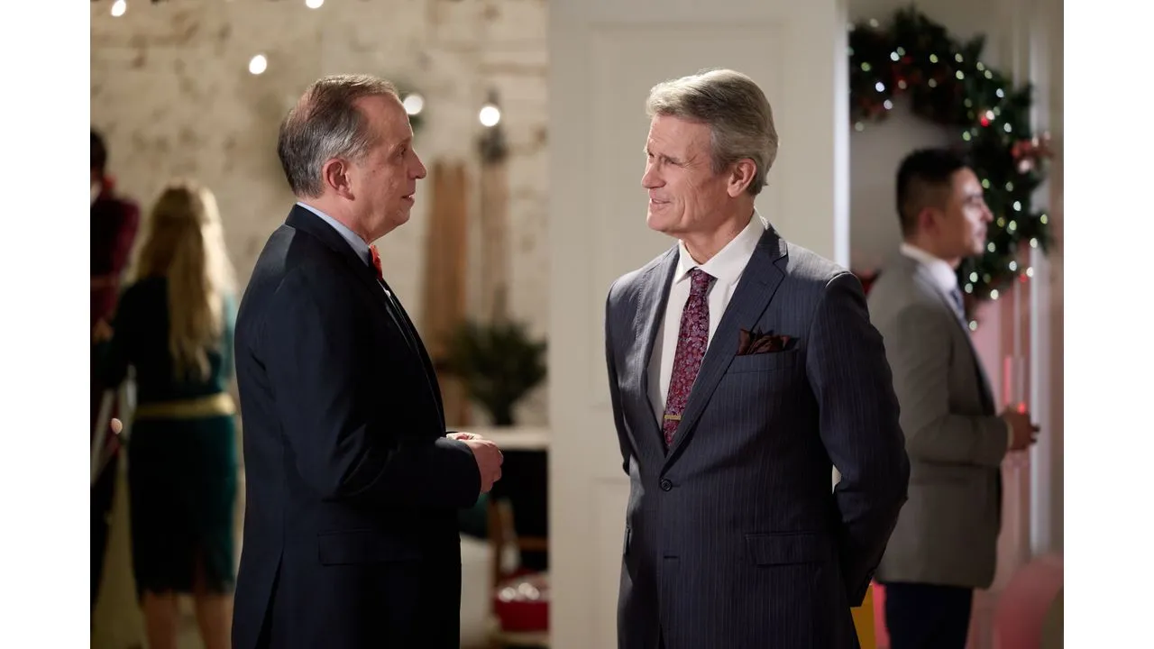 Two men in suits chat at a festive indoor party with Christmas lights in the background