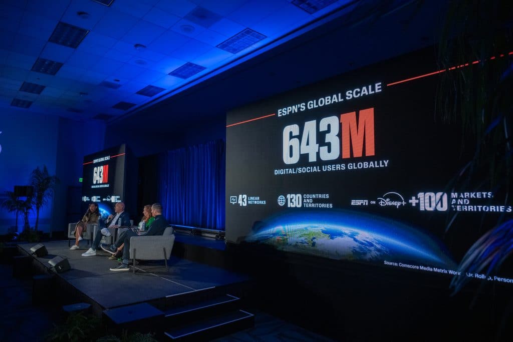 Panel of speakers on a stage beside a large screen showing ESPNs Global Scale 643M at a conference