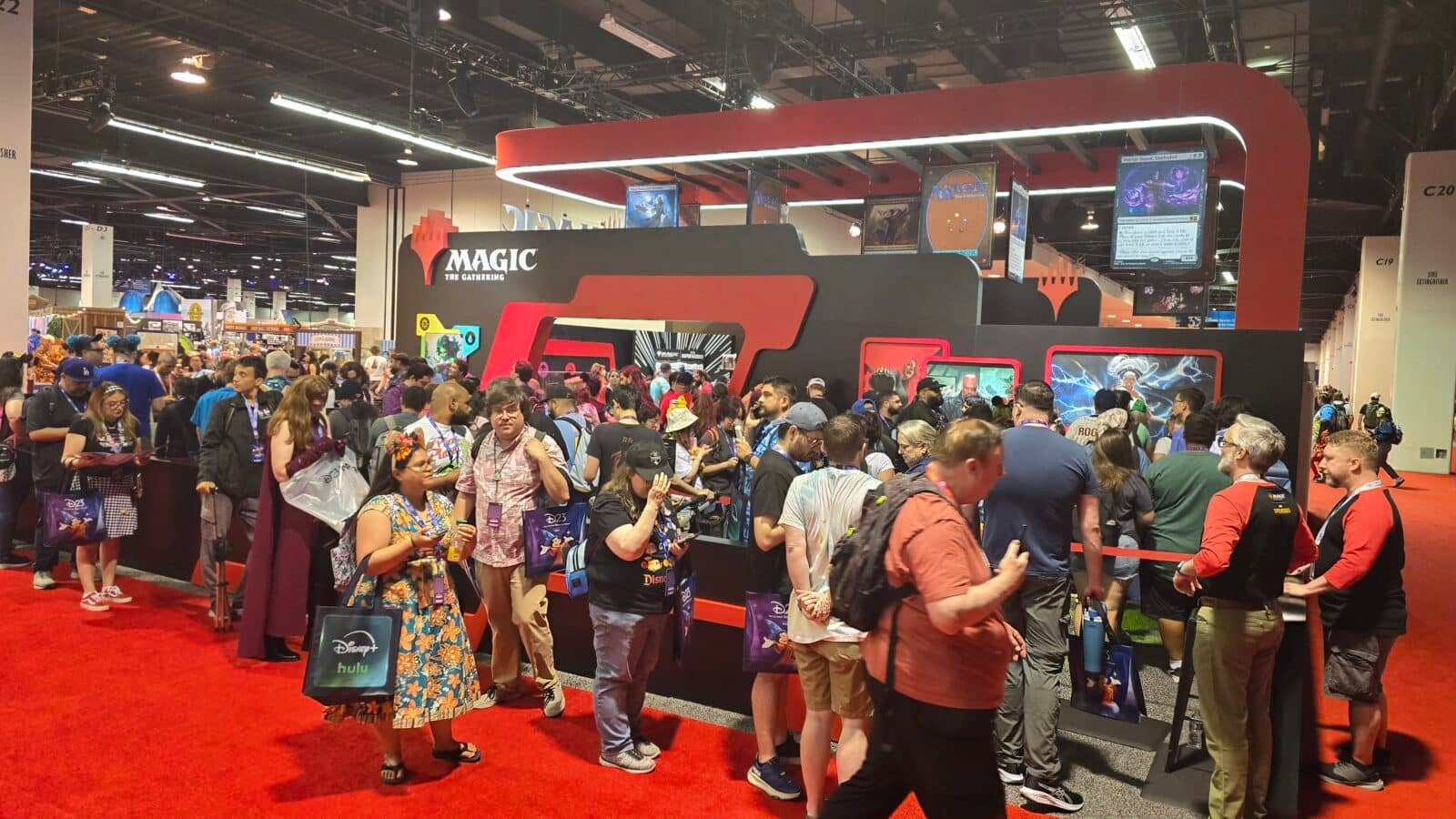 Crowded convention floor with a large Magic The Gathering booth and red and black display walls