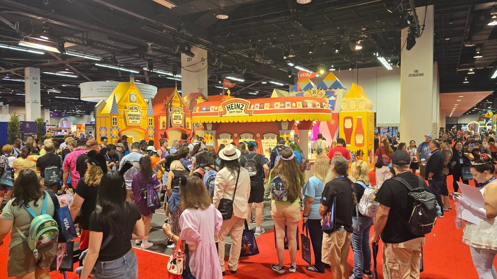 Busy convention hall with a large Heinz branded inflatable booth and colorful structures surrounded by attendees